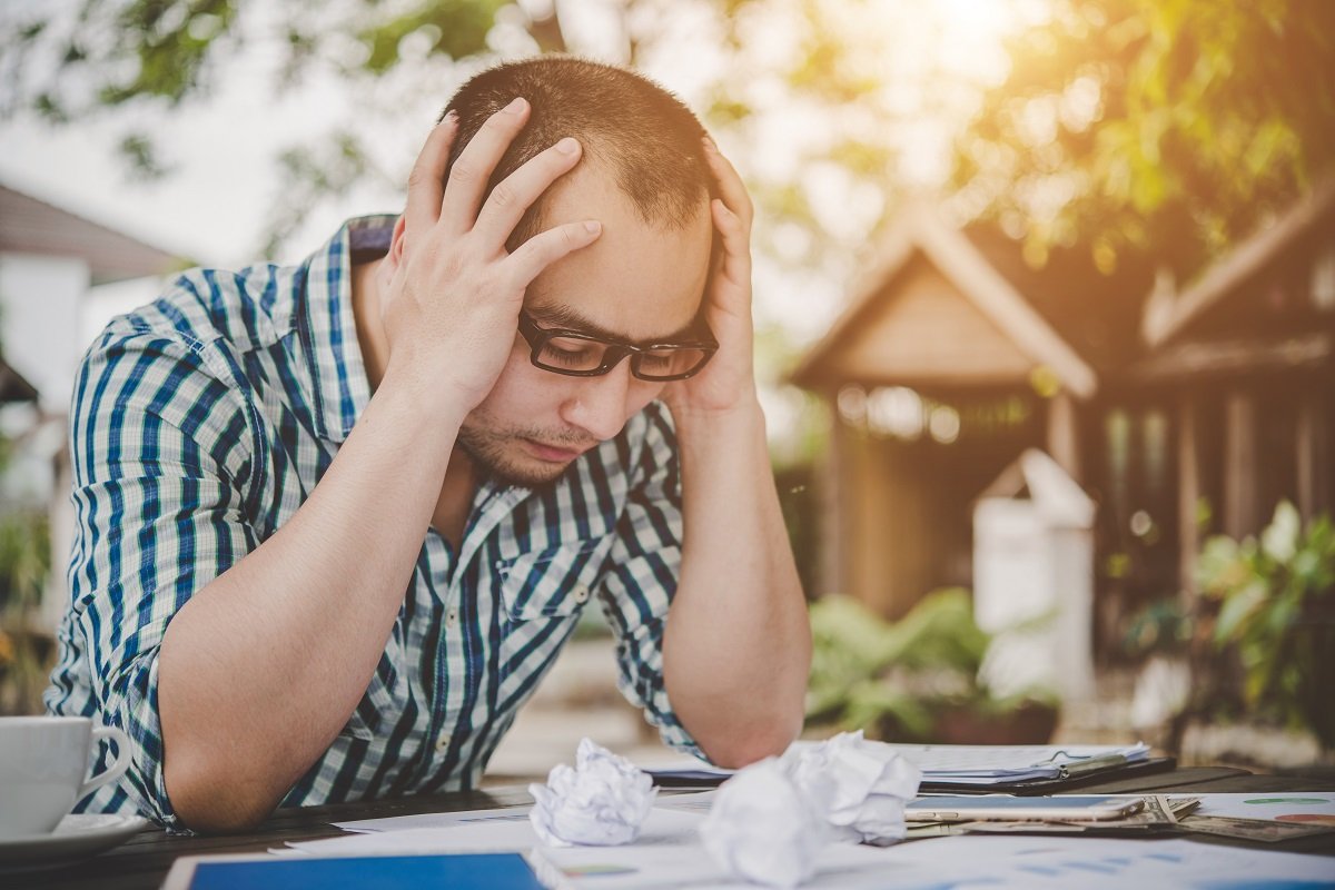 Stressed businessman with papers and charts sitting at table at
